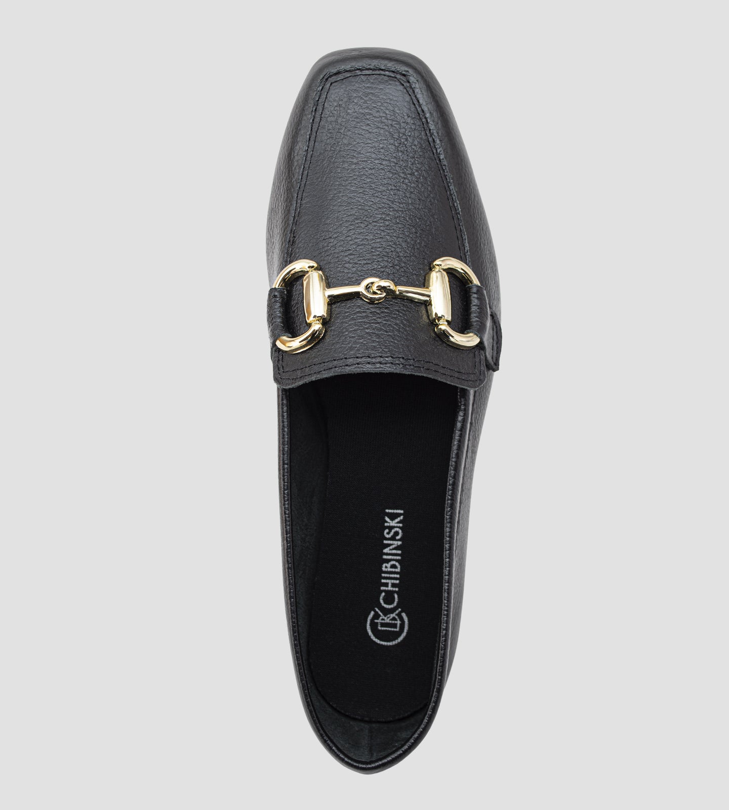 Mocassim feminino preto em couro legítimo com detalhe metálico dourado frontal e solado baixo, usado com calça clara em composição elegante e sofisticada.