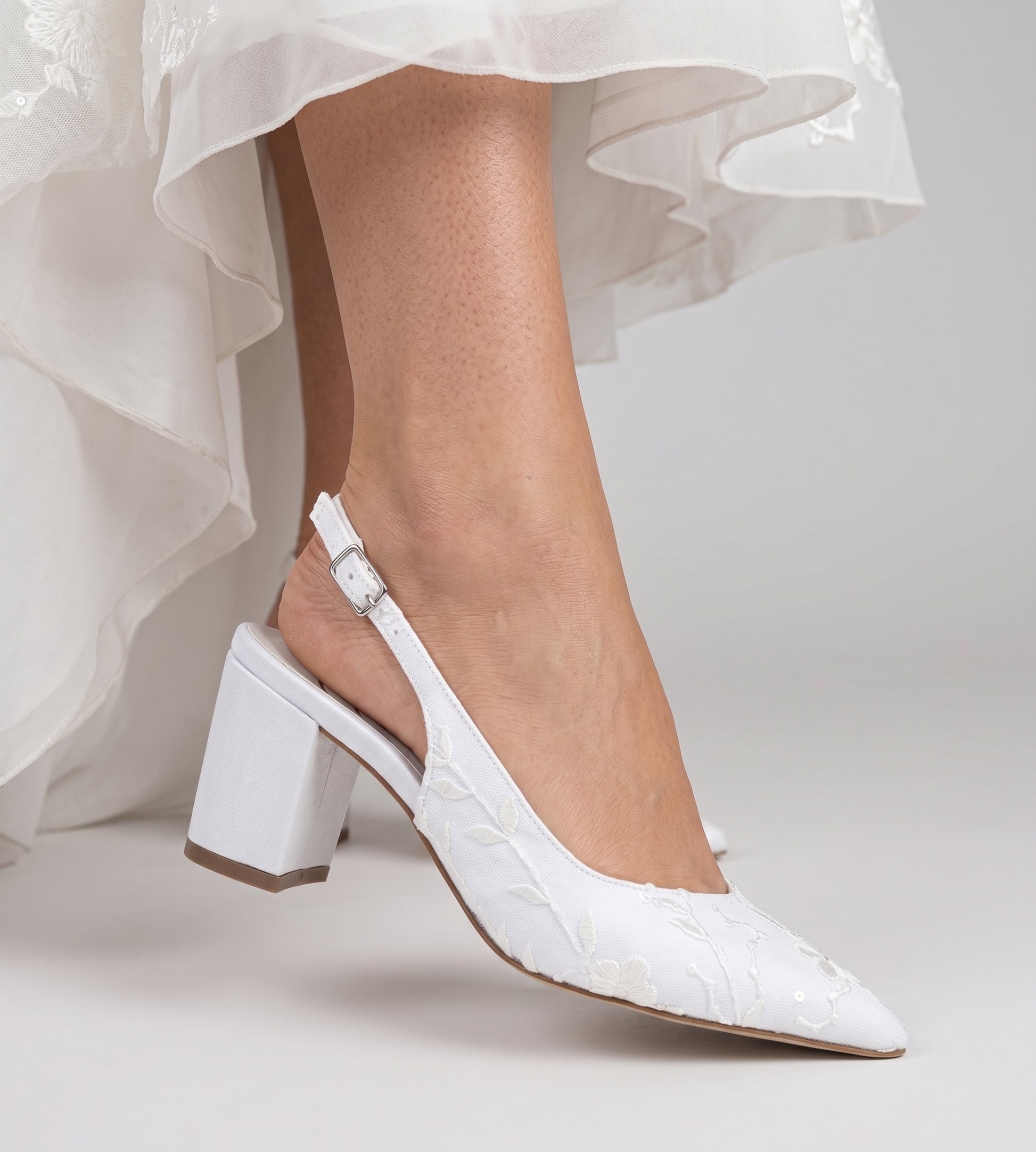 Sapato de noiva slingback em renda branca com flores bordadas, bico fino, salto bloco médio e tira ajustável no calcanhar, ideal para casamentos, combinando elegância, conforto e acabamento artesanal.