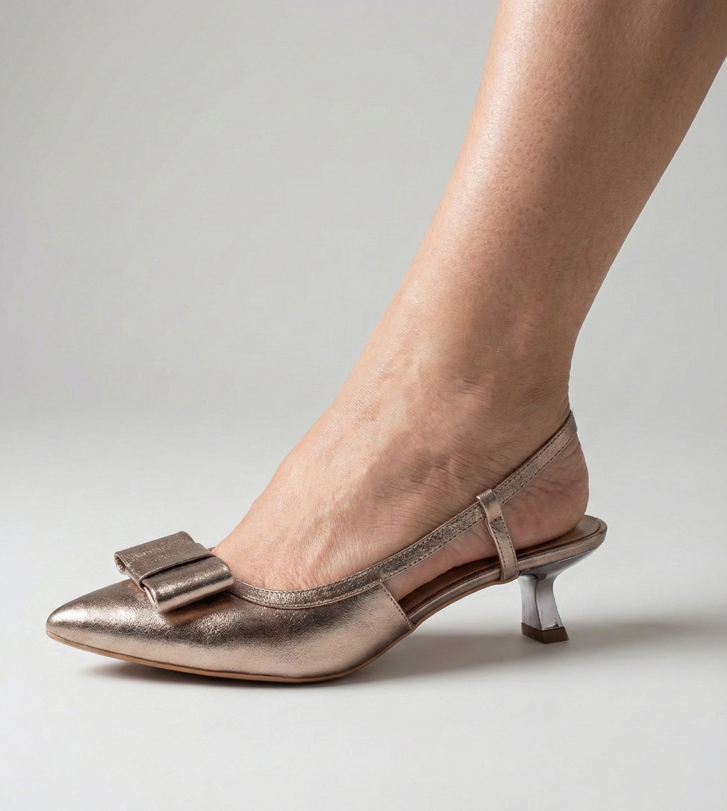 Scarpin slingback em couro metalizado dourado, com laço decorativo na parte frontal e salto taça de 5cm. Modelo elegante e sofisticado, ideal para festas e eventos especiais.