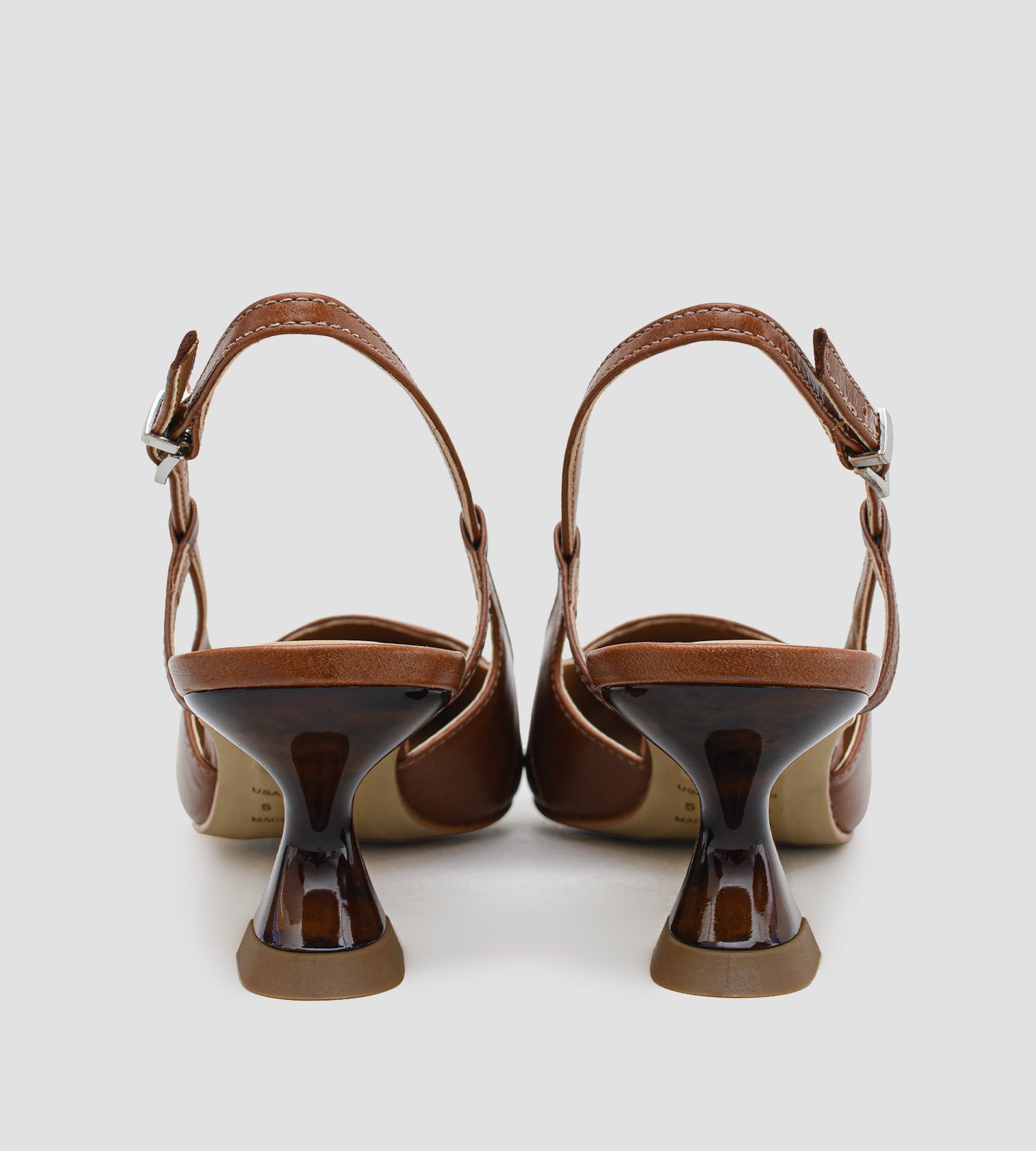 Fotografia de um par de sapatos femininos modelo scarpin slingback na cor caramelo sobre um fundo claro. O calçado possui bico fino com a ponta envernizada em estampa de tartaruga, além de um salto escultural de 6 centímetros com o mesmo padrão de tartaruga. O fechamento é feito por uma tira fina com fivela prateada ajustável no calcanhar.