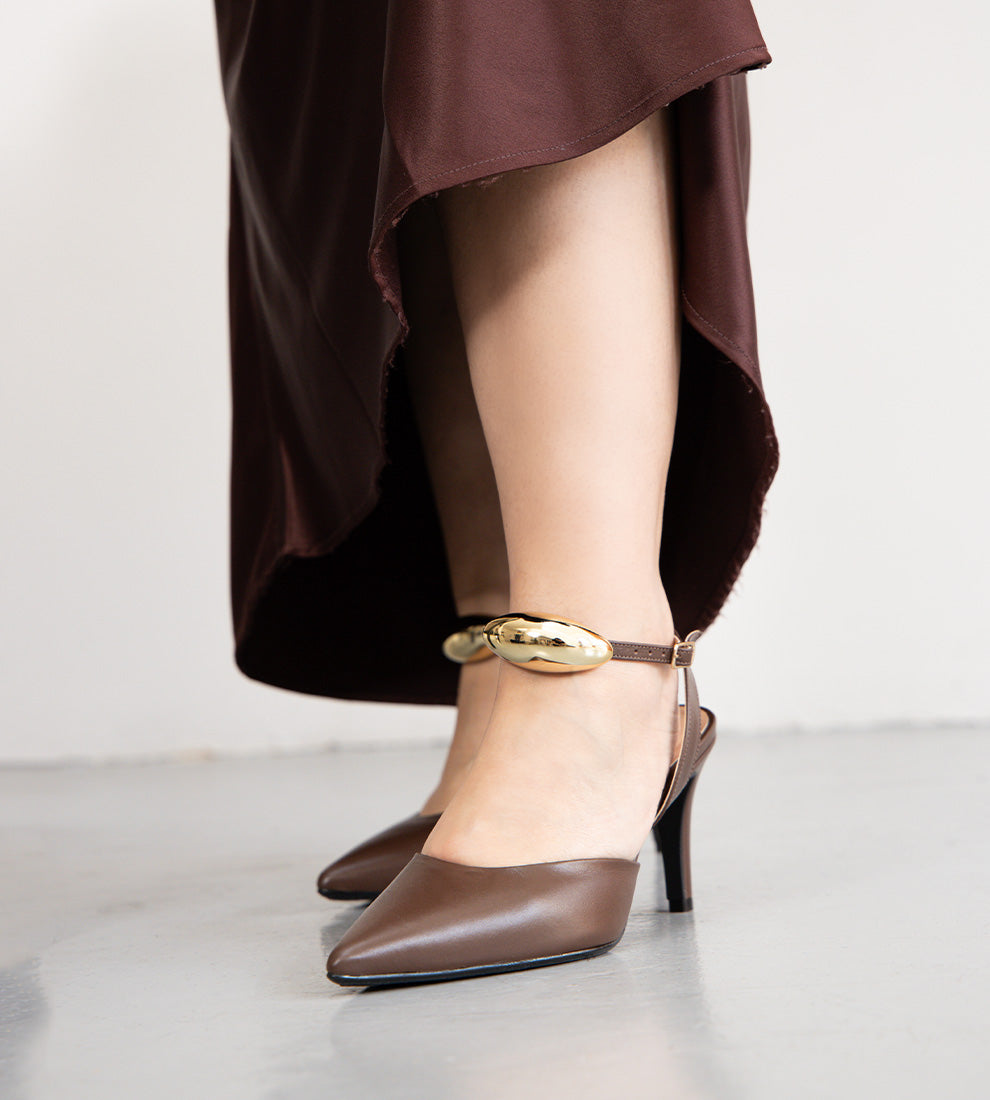 Sandália scarpin marrom em couro com salto fino de 9cm, bico fino e tornozeleira ajustável com detalhe metálico dourado removível.