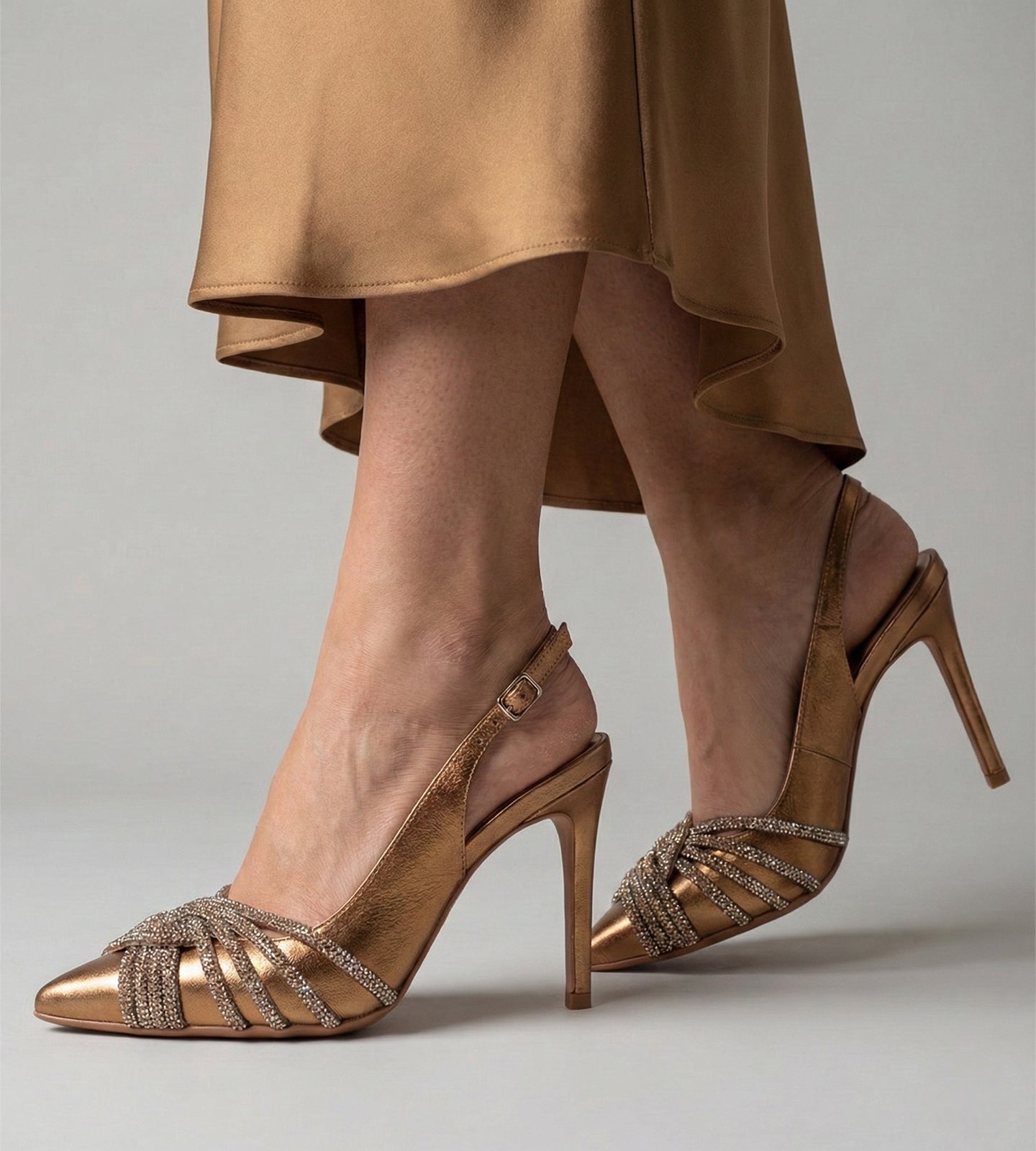 Scarpin feminino bronze em couro legítimo com bico fino, salto alto fino de 10 cm, modelo slingback com fivela e tiras frontais com aplicação de strass, ideal para festas e eventos formais.