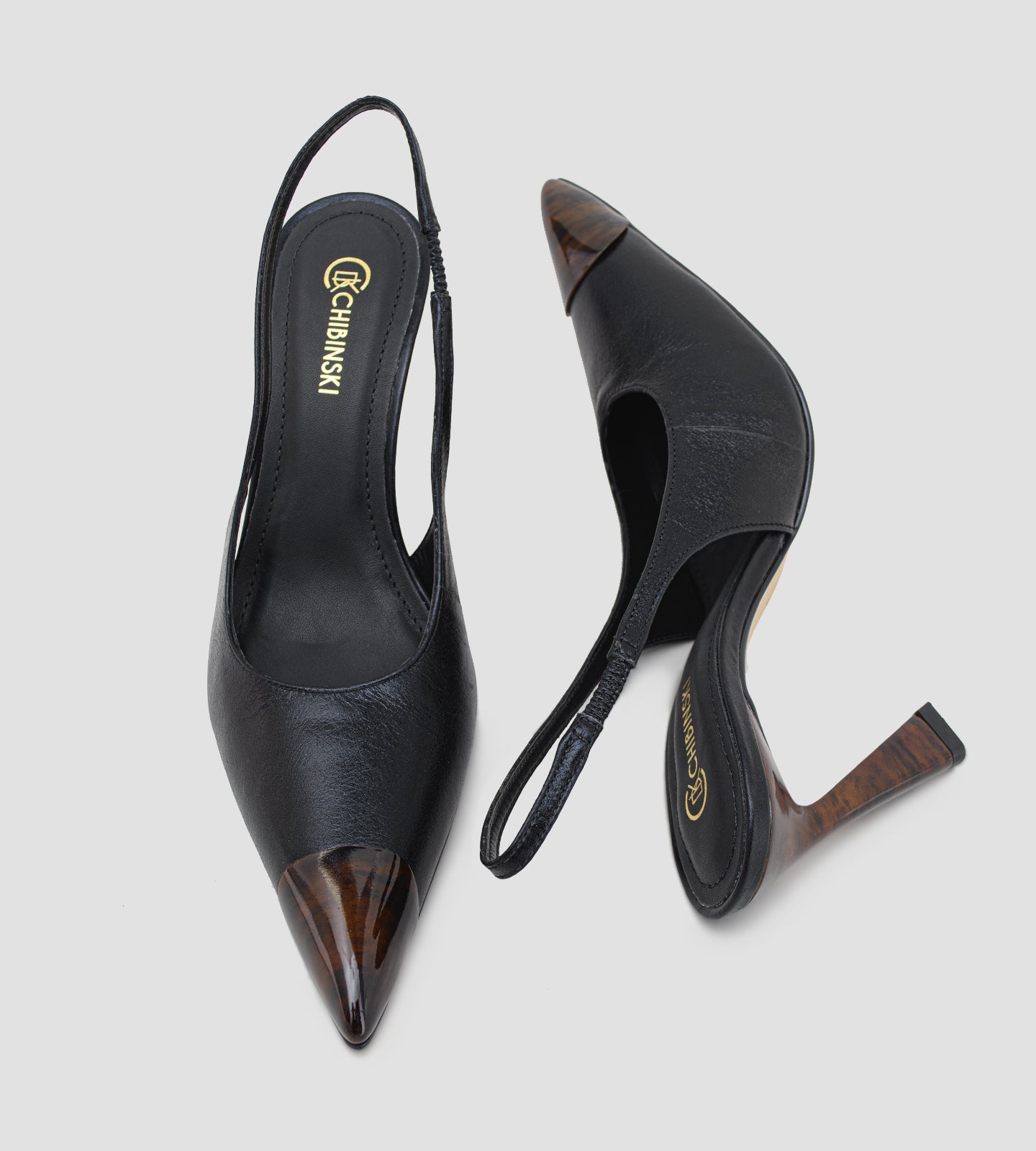Scarpin slingback feminino de couro preto com salto alto fino de 10 cm, bico fino com ponteira marrom e tira no calcanhar, modelo elegante para trabalho, eventos e ocasiões formais.