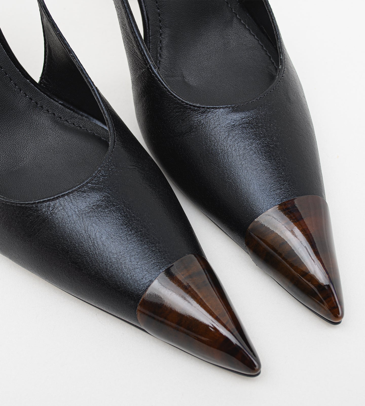 Scarpin slingback feminino de couro preto com salto alto fino de 10 cm, bico fino com ponteira marrom e tira no calcanhar, modelo elegante para trabalho, eventos e ocasiões formais.