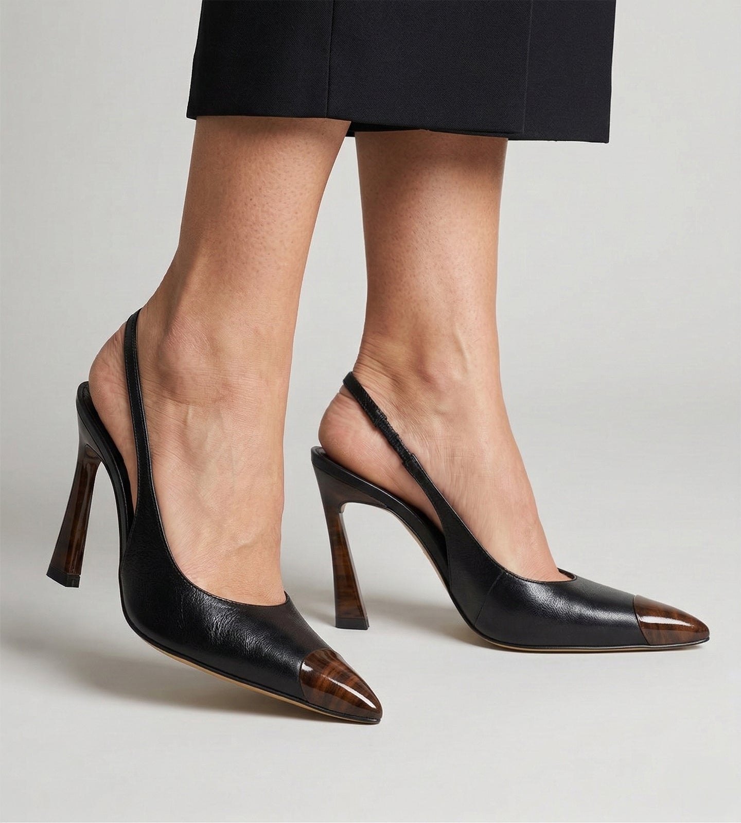 Scarpin slingback feminino de couro preto com salto alto fino de 10 cm, bico fino com ponteira marrom e tira no calcanhar, modelo elegante para trabalho, eventos e ocasiões formais.