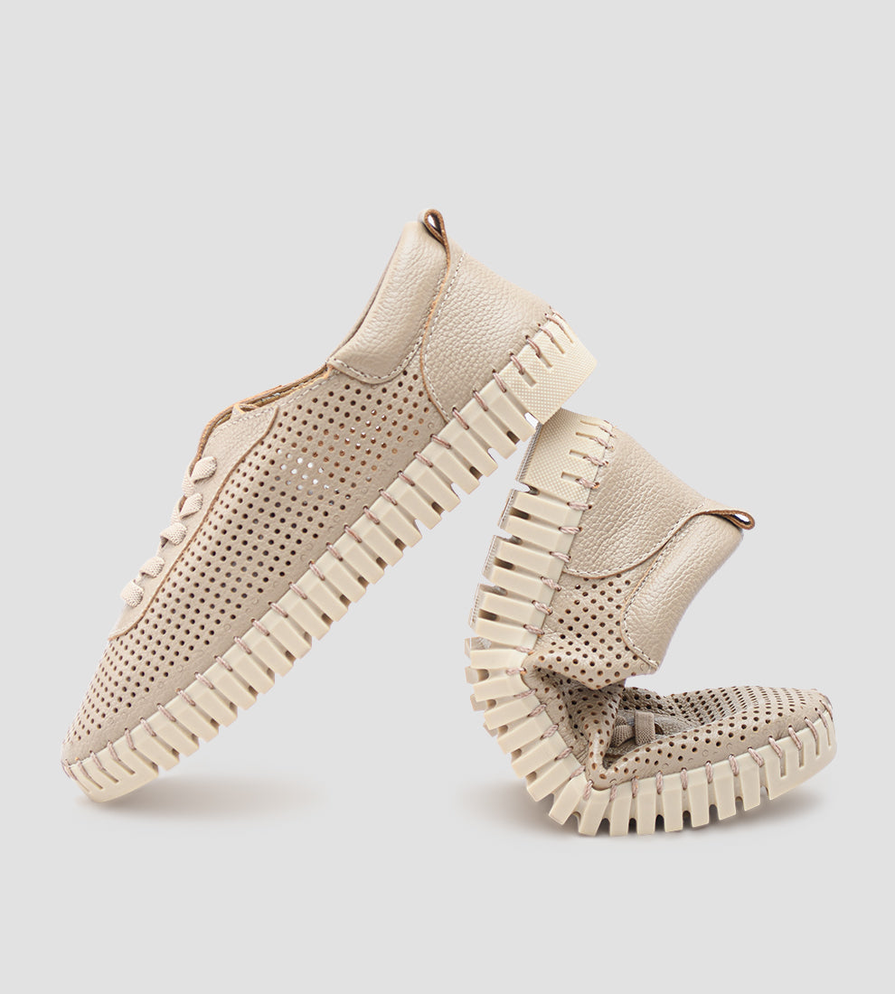 Tênis Feminino Casual na cor nude/bege claro, com o cabedal totalmente perfurado e cadarços finos. O tênis possui solado flexível estilo driving shoe, emborrachado e costurado, com um dos pés dobrado para demonstrar a alta flexibilidade.