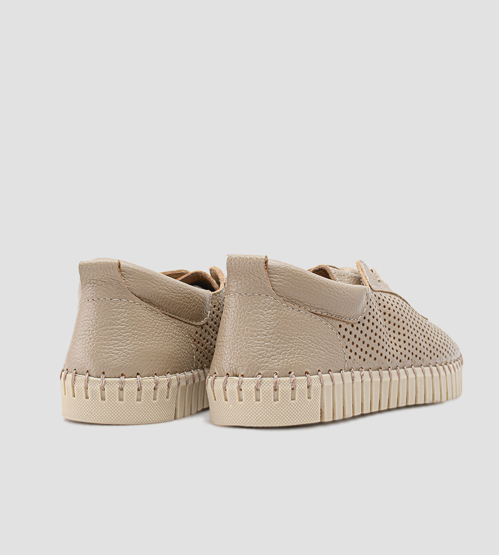 Tênis Feminino Casual na cor nude/bege claro, com o cabedal totalmente perfurado e cadarços finos. O tênis possui solado flexível estilo driving shoe, emborrachado e costurado, com um dos pés dobrado para demonstrar a alta flexibilidade.