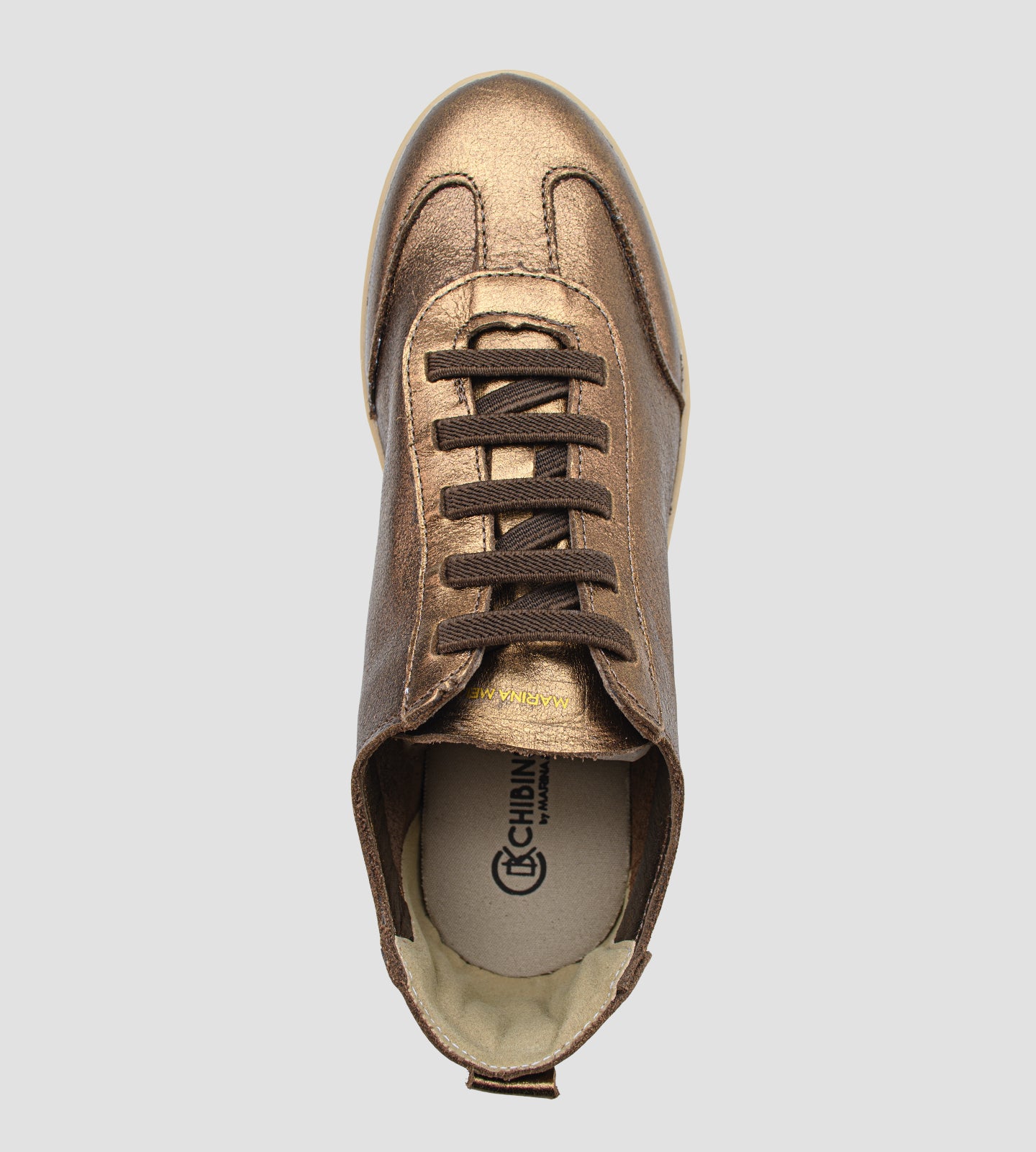 Tênis feminino em couro legítimo bronze metalizado da coleção Chibinski by Marina Mello, com cadarço marrom, solado emborrachado bege e palmilha em gel para maior conforto.
