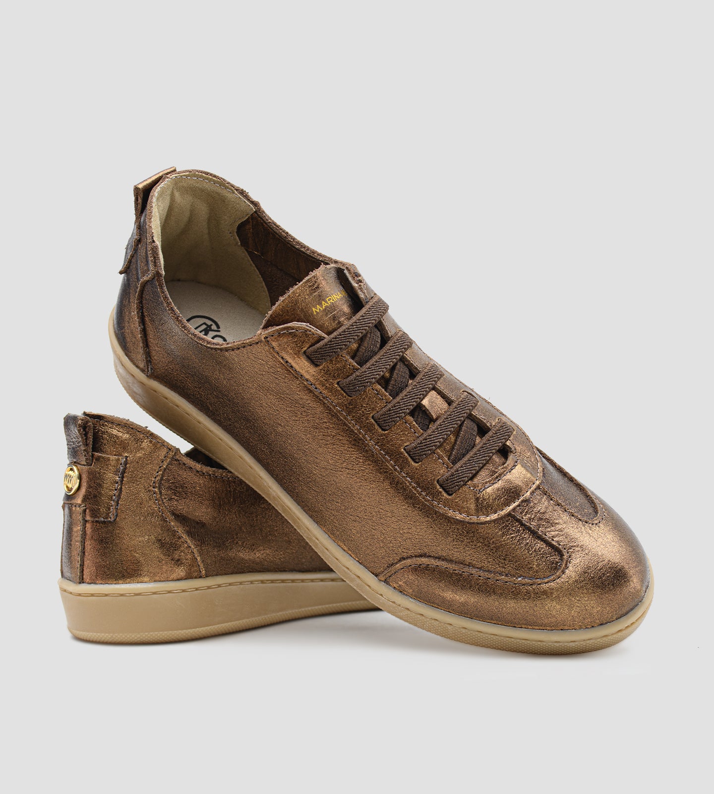 Tênis feminino em couro legítimo bronze metalizado da coleção Chibinski by Marina Mello, com cadarço marrom, solado emborrachado bege e palmilha em gel para maior conforto.