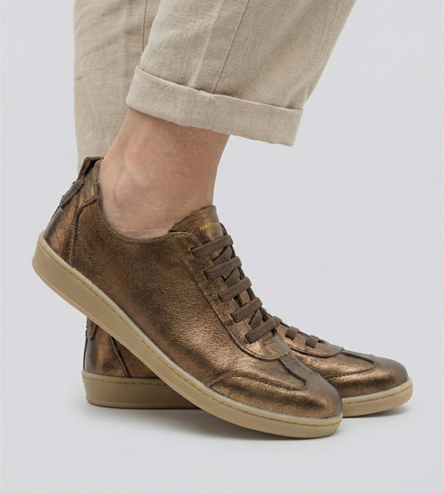 Tênis feminino em couro legítimo bronze metalizado da coleção Chibinski by Marina Mello, com cadarço marrom, solado emborrachado bege e palmilha em gel para maior conforto.