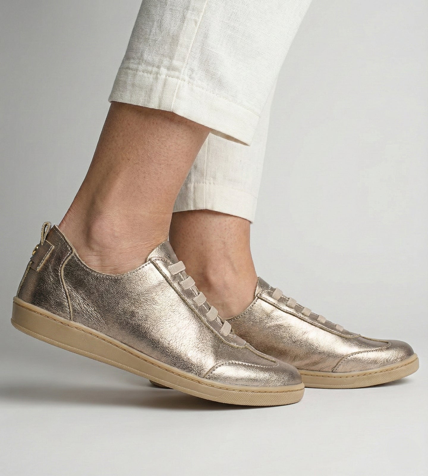 Tênis feminino em couro legítimo dourado metalizado da coleção Chibinski by Marina Mello, com cadarço marrom, solado emborrachado bege e palmilha em gel para maior conforto.