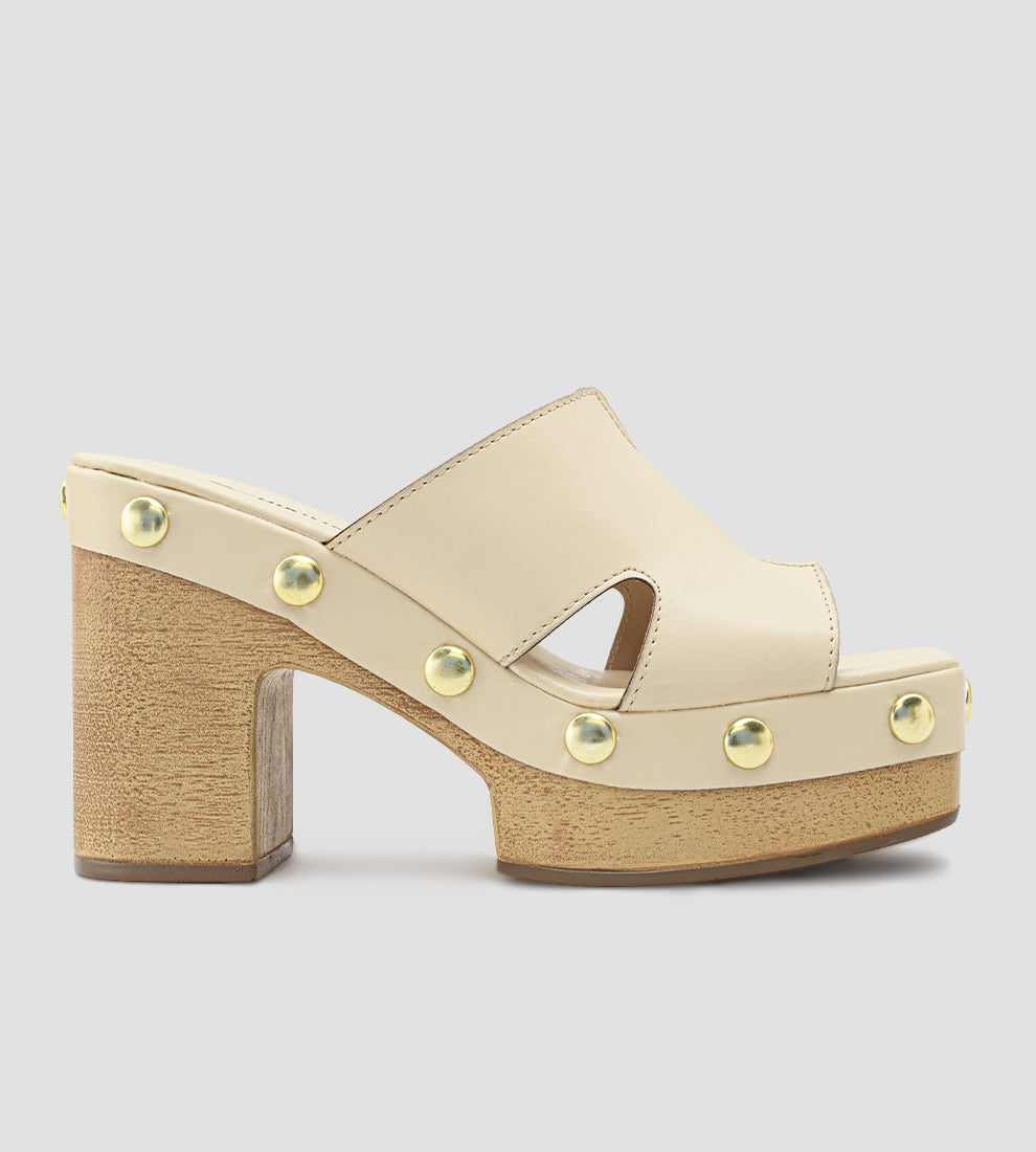 Tamanco plataforma nude feminino com salto bloco em madeira, cabedal com recortes laterais e tachinhas douradas decorativas ao redor da base.