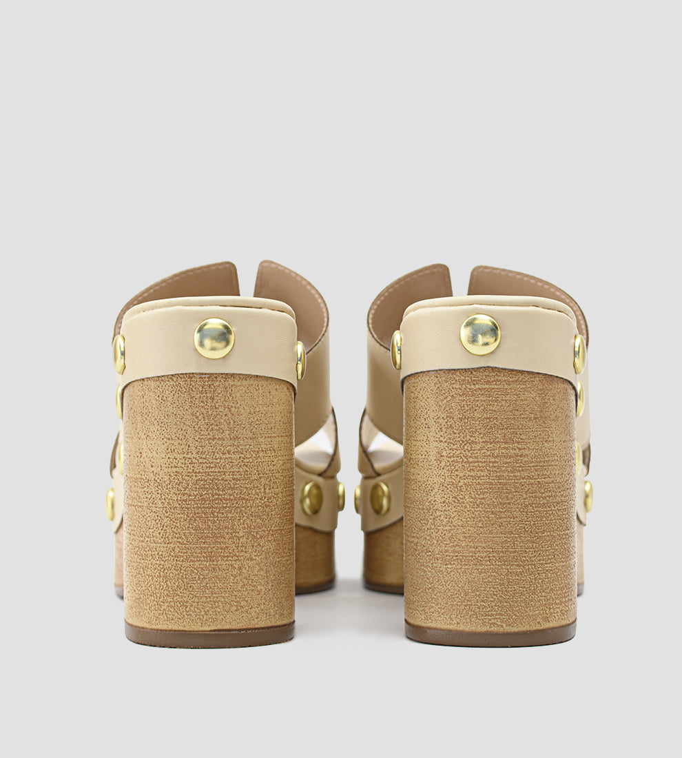 Tamanco plataforma nude feminino com salto bloco em madeira, cabedal com recortes laterais e tachinhas douradas decorativas ao redor da base.