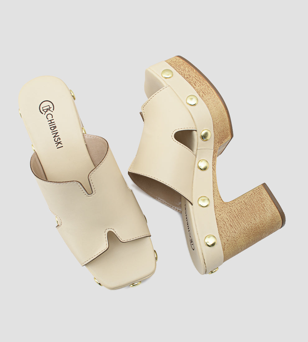 Tamanco plataforma nude feminino com salto bloco em madeira, cabedal com recortes laterais e tachinhas douradas decorativas ao redor da base.