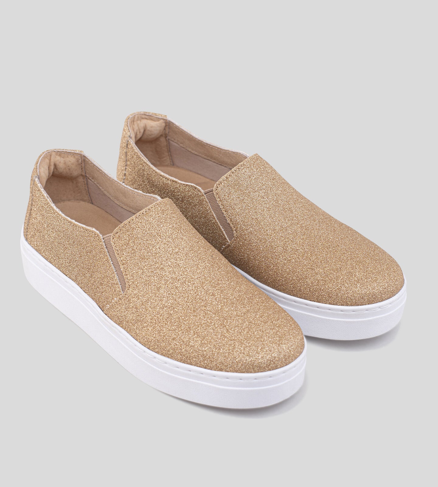 Tênis slip-on com acabamento em glitter dourado, apresentando um design elegante e moderno. O calçado possui um cabedal suave e uma sola branca, ideal para compor looks casuais e festivos. A textura brilhante do glitter adiciona um toque de glamour, tornando-o perfeito para ocasiões especiais ou para dar um charme extra ao dia a dia.