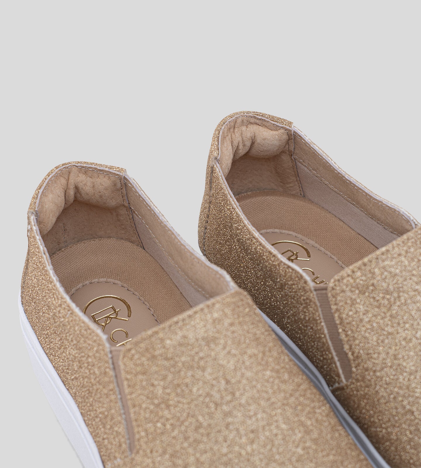 Tênis slip-on com acabamento em glitter dourado, apresentando um design elegante e moderno. O calçado possui um cabedal suave e uma sola branca, ideal para compor looks casuais e festivos. A textura brilhante do glitter adiciona um toque de glamour, tornando-o perfeito para ocasiões especiais ou para dar um charme extra ao dia a dia.